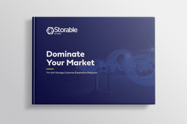 A book with a dark blue cover titled "Dominate Your Market: The Self-Storage Customer Experience Playbook" by Storable.